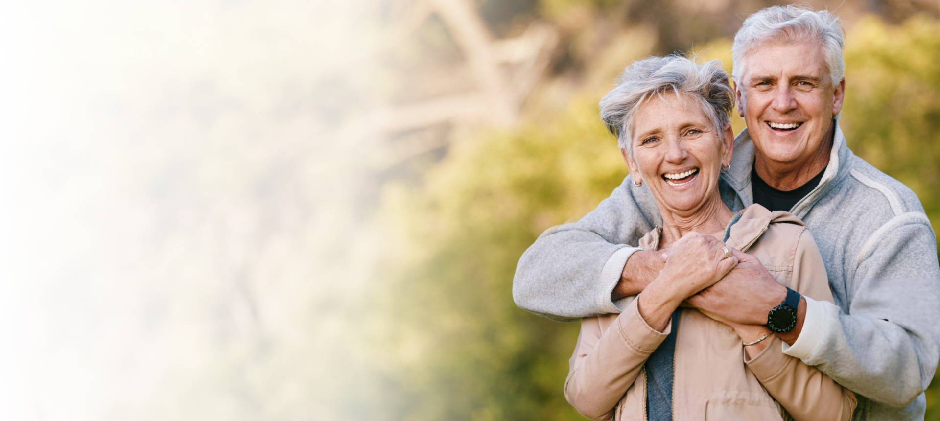 Happy senior couple smiling outdoors in natural daylight, embracing warmly together.