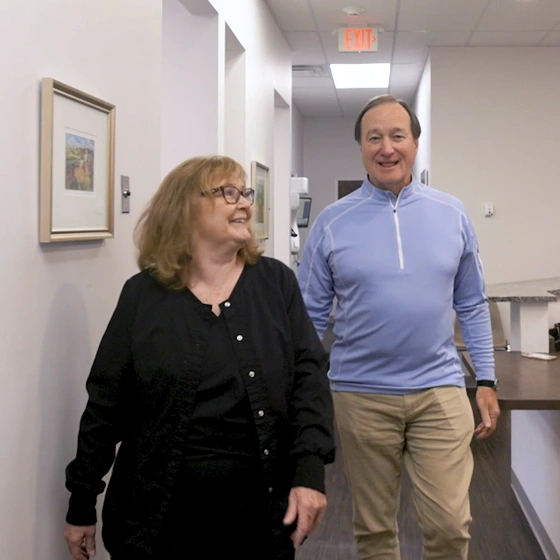 Two people walking together in a bright dental office hallway with framed artwork on walls.